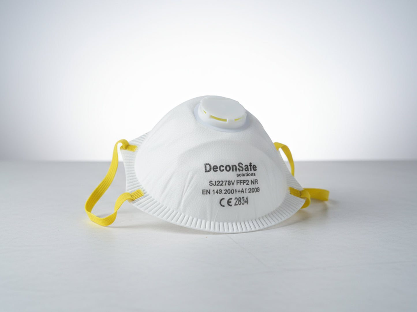 A white DeconSafe Solutions FFP2 protective respirator mask with a yellow strap and a breathing valve.