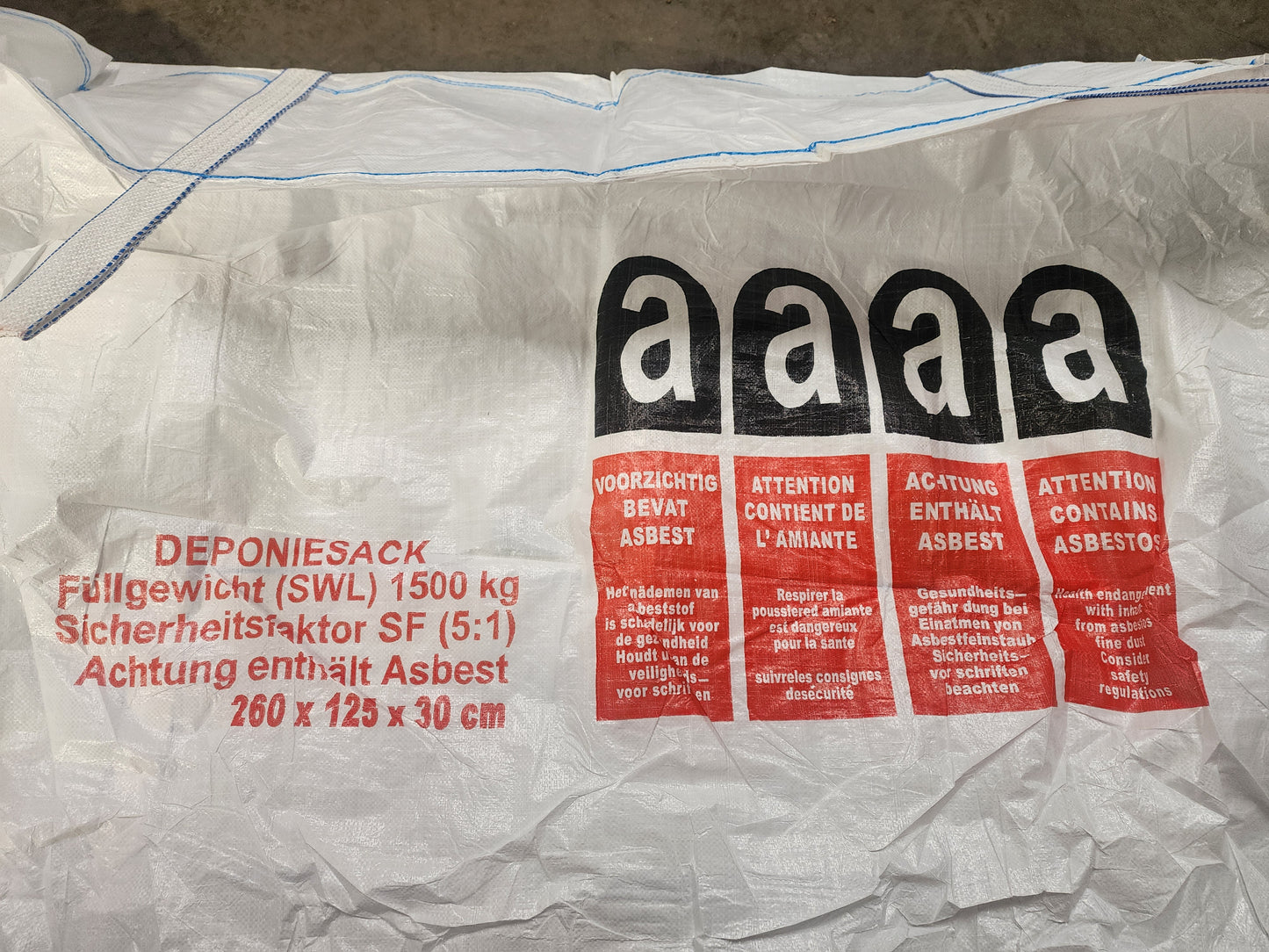 A white industrial waste bag with hazard warnings in multiple languages stating that it contains asbestos.