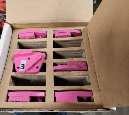 A cardboard box containing several pink industrial diamond grinding segments, with one segment in the foreground featuring a large white label with the number "3".