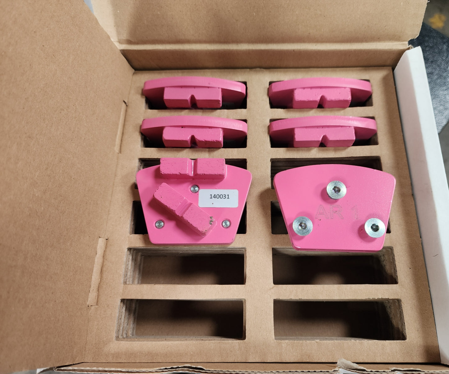 A box containing several pink, fan-shaped grinding segments for a concrete floor grinder, with one piece labeled "140031" and another marked "AR 1."