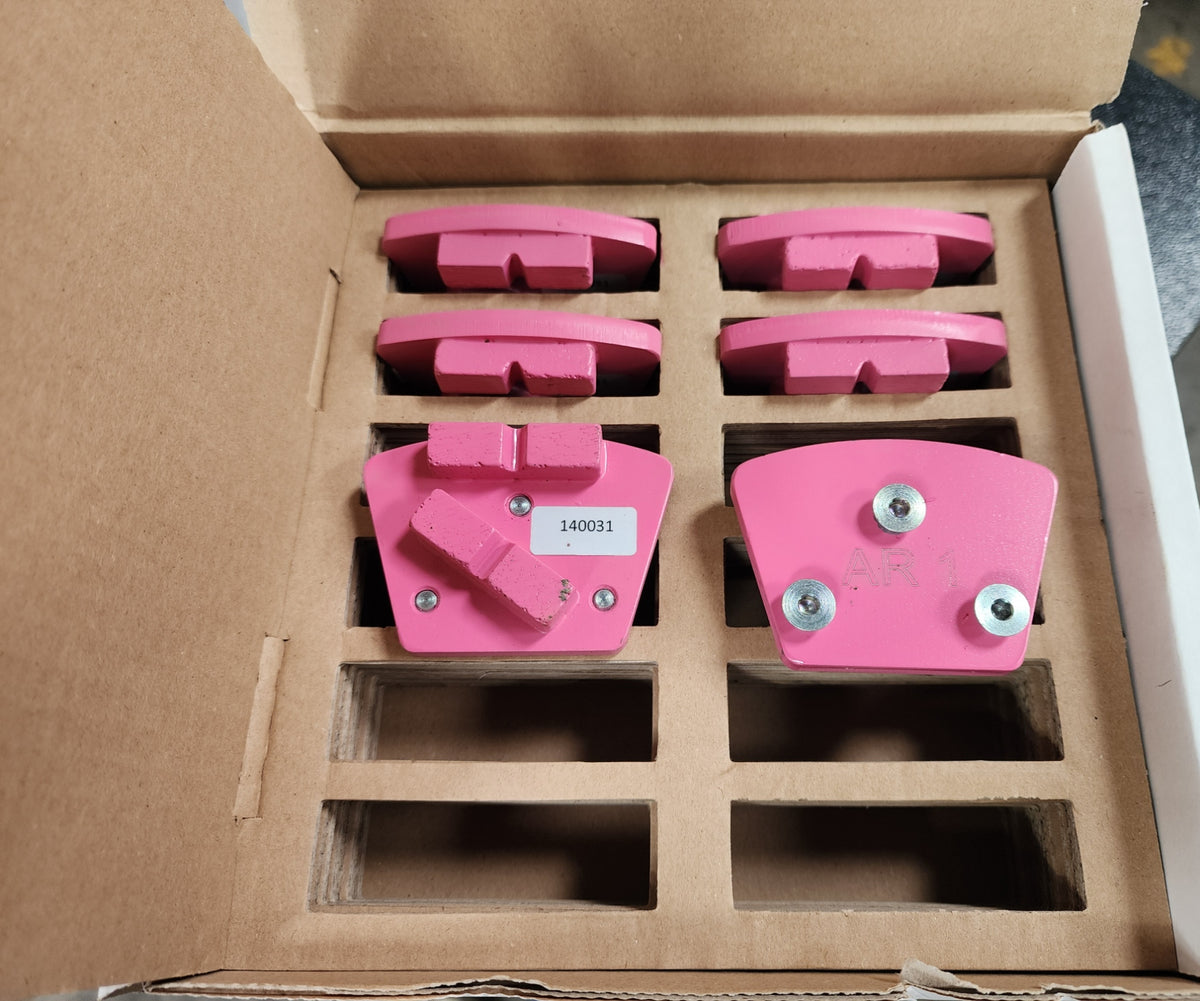 A box containing several pink, fan-shaped grinding segments for a concrete floor grinder, with one piece labeled "140031" and another marked "AR 1."