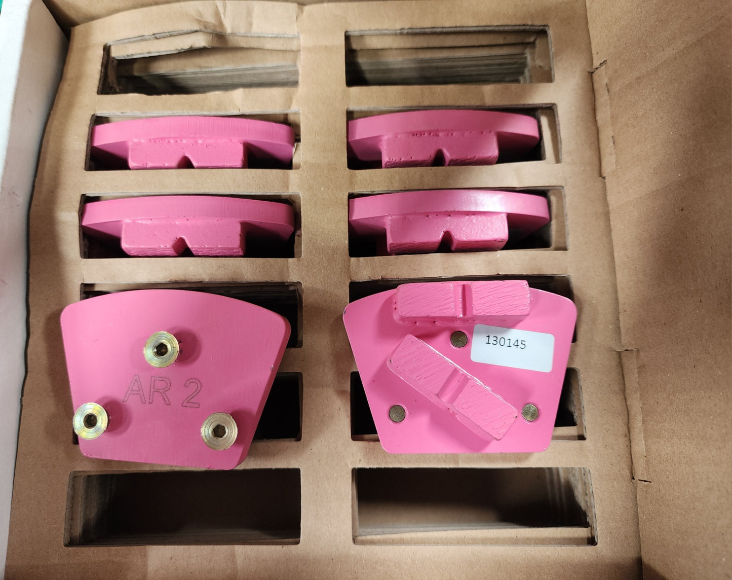 A cardboard box containing pink industrial diamond grinding segments, with one segment in the foreground labeled "AR 2" and another labeled with the code "130145".