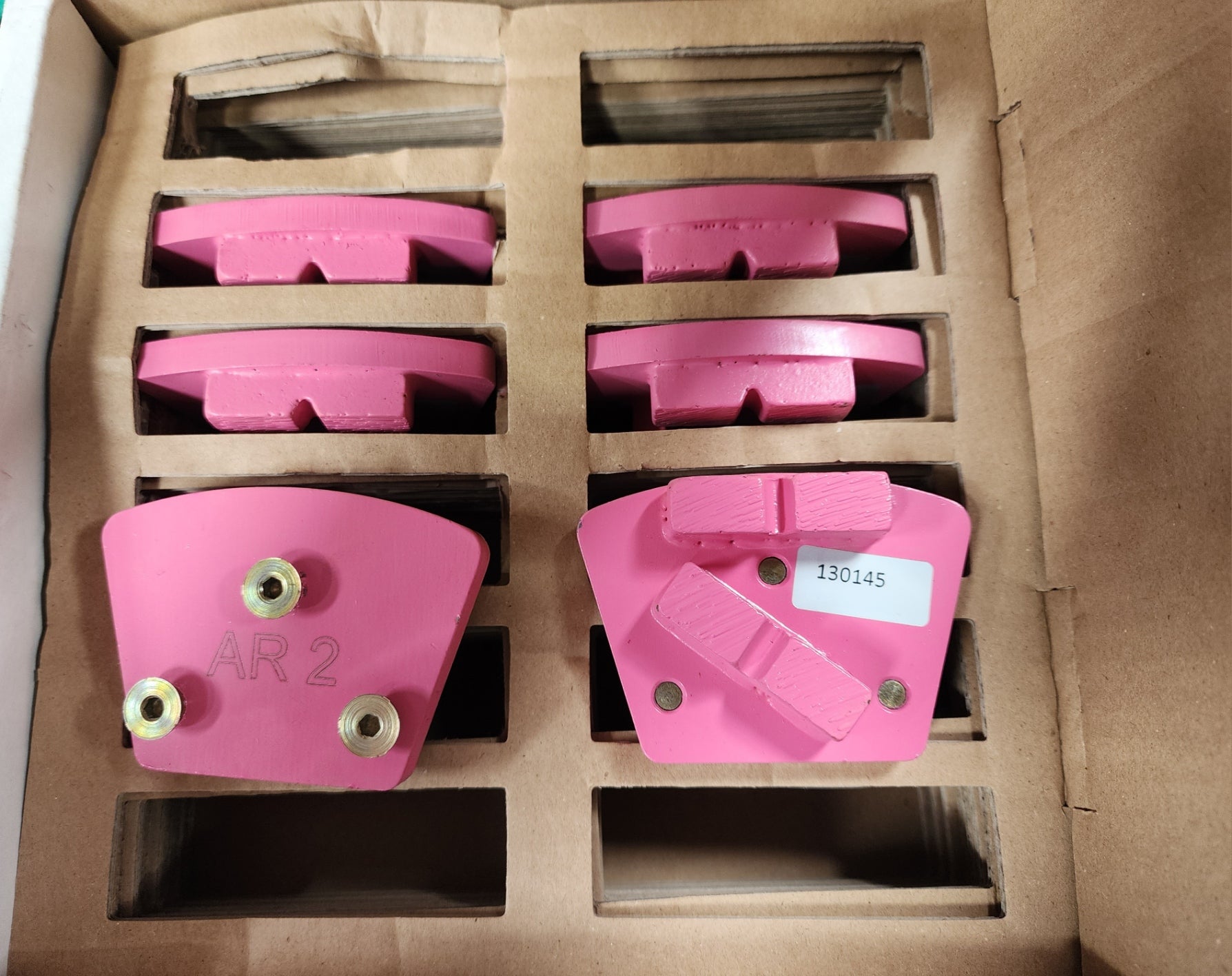 A cardboard box containing pink industrial diamond grinding segments, with one segment in the foreground labeled "AR 2" and another labeled with the code "130145".