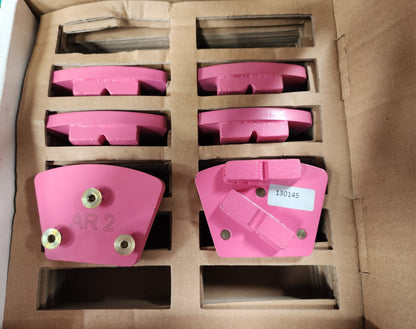 A cardboard box containing pink industrial diamond grinding segments, with one segment in the foreground labeled "AR 2" and another labeled with the code "130145".