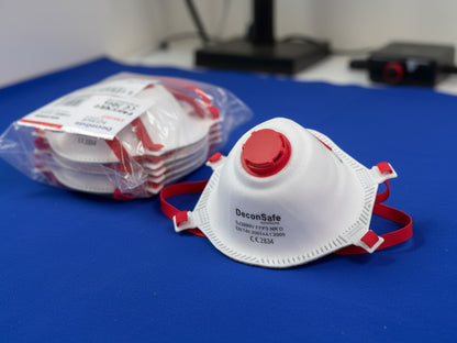 A white DeconSafe Solutions FFP3 protective respirator mask with a red breathing valve and matching red straps, sitting next to a sealed pack of identical masks.