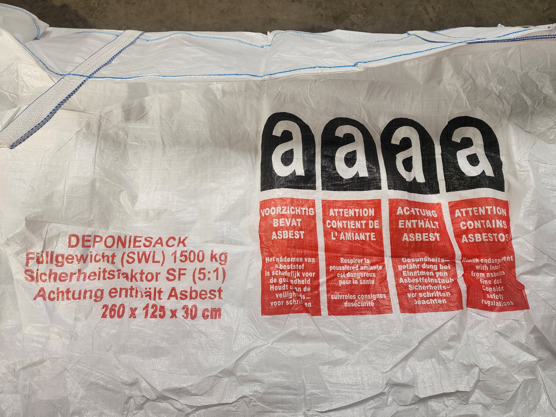 A white industrial waste bag with hazard warnings in multiple languages stating that it contains asbestos.