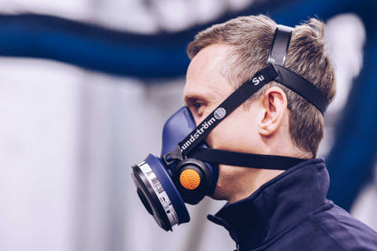 A side profile of a man wearing a blue Sundström SR 100 half-mask respirator with a black head harness strap.